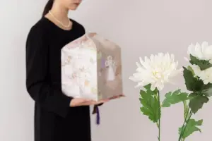 骨壺を抱える喪服の女性と白菊